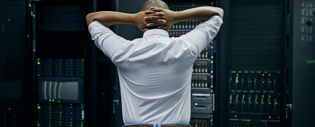 Male IT technician looking at server rack with hands behind head